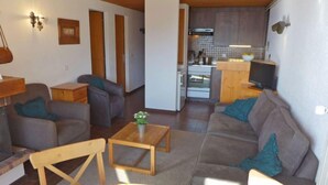 A modern living room with a sofa, chairs, and a dining table. There is a kitchen area with a stove and a television. - La Vire D'Aufalle 14 Inférieur by Interhome (Alpe des Chaux)