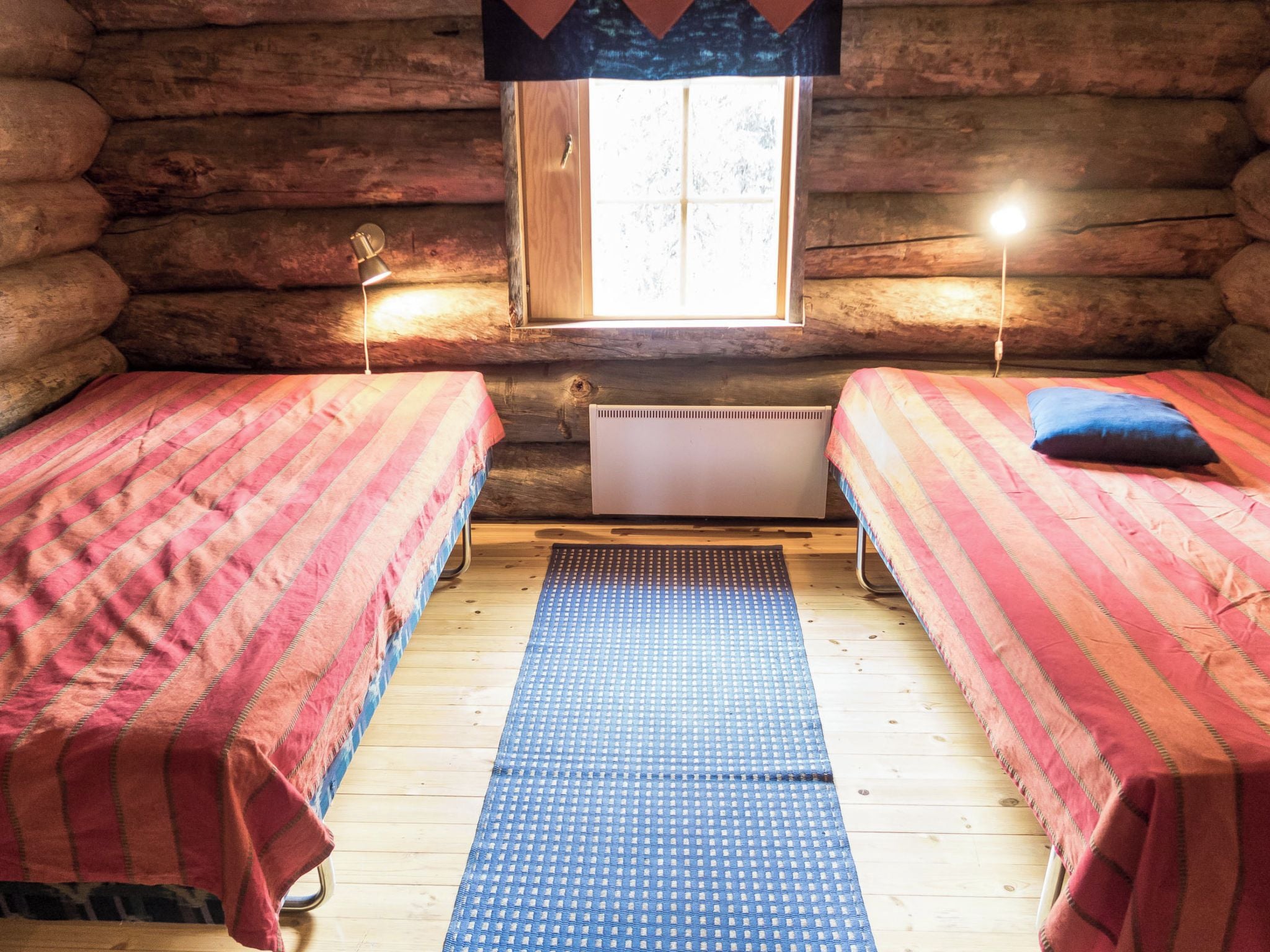 A log cabin room with two beds, a window, and a radiator.