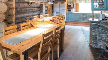 Una mesa de comedor de madera rústica con sillas, una chimenea de piedra y una zona de cocina con armarios y electrodomésticos.