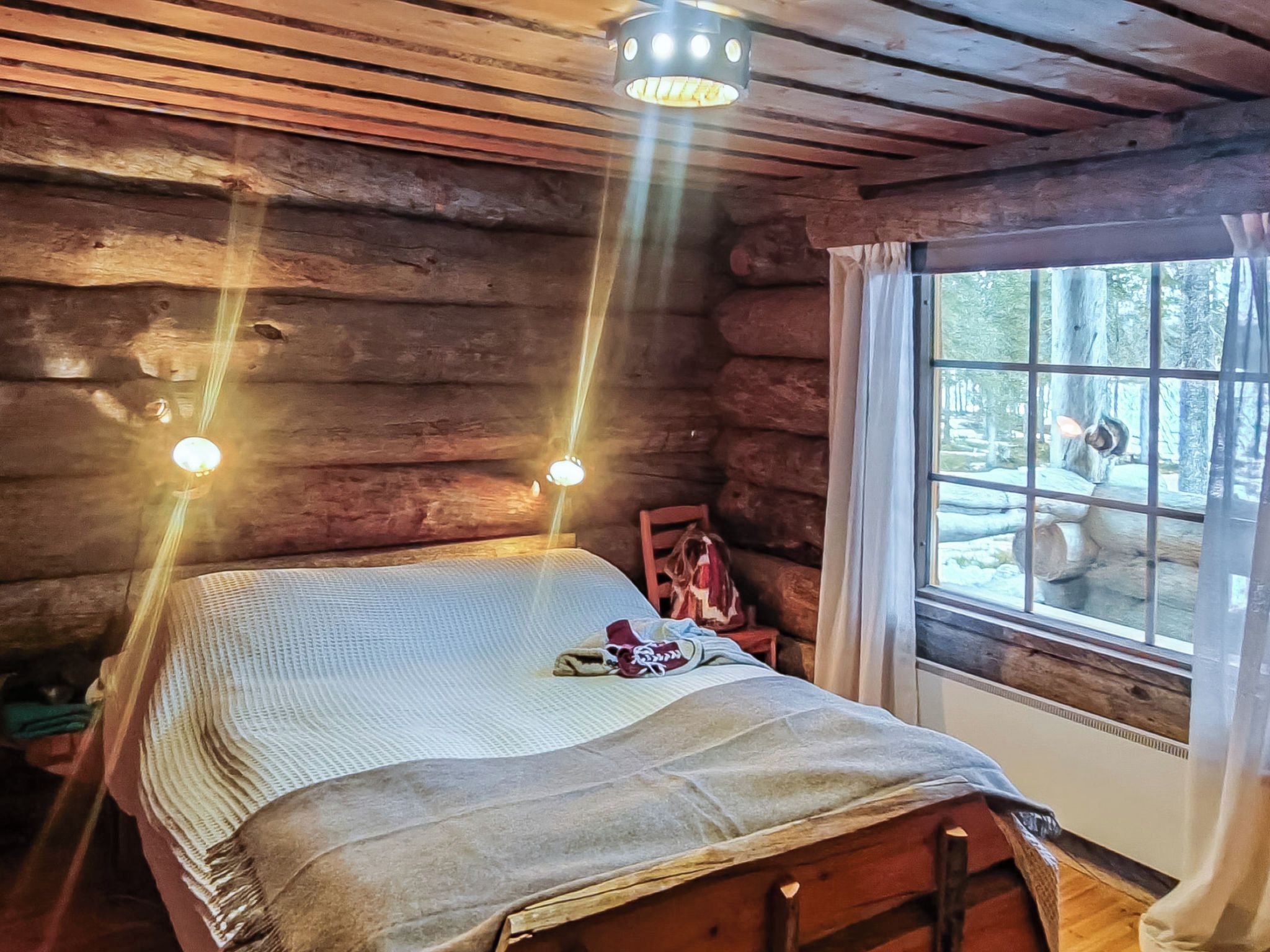 Un dormitorio tipo cabaña de madera con una cama de madera, una ventana con cortinas y vistas al exterior.