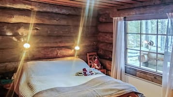 Un dormitorio tipo cabaña de madera con una cama de madera, una ventana con cortinas y vistas al exterior.