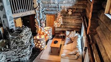 Interior de una cabaña de troncos con pared de piedra, escalera de madera, sofá e iluminación colgante.