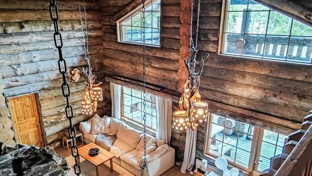 A log cabin interior with a sofa, dining table, and hanging lights.