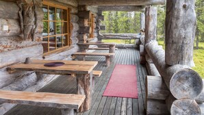 A rustic wooden cabin with a porch, wooden benches, and a red mat.