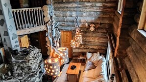 A cozy log cabin interior with a stone fireplace, a sofa, and hanging lights.