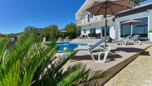 En moderne villa med pool, udendørs møbler og en balkon med udsigt over poolen.