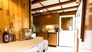 Un interior de madera con una mesa y sillas de comedor, una zona de cocina con armarios de madera y un refrigerador.