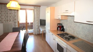A compact kitchen with a stove, sink, and a dining area with a table and chairs. - Jägerhof by Interhome (Schwaz)