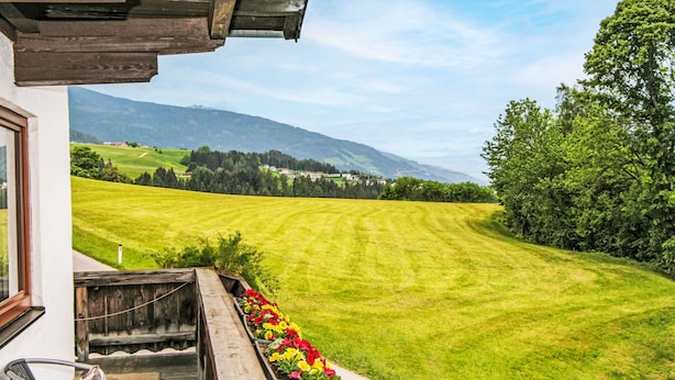A view from a balcony overlooking a well-maintained lawn with a row of colorful flowers, a wooden deck, and a mountain landscape in the distance. - Jägerhof by Interhome (Schwaz)