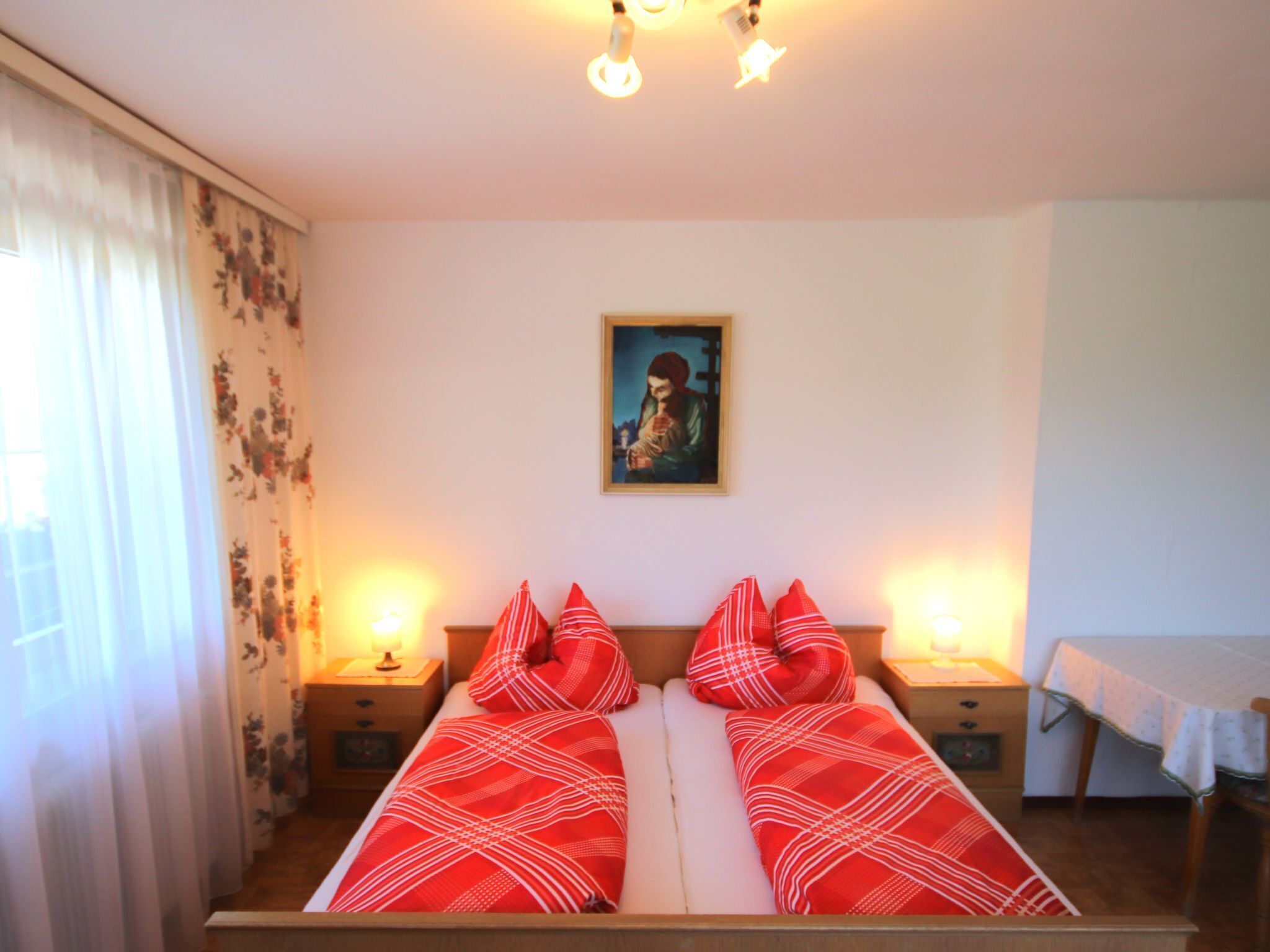 A room with two single beds, a painting on the wall, and a table with a tablecloth.