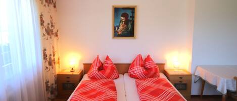 A room with two single beds, a painting on the wall, and a table with a tablecloth.
