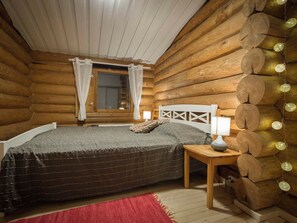 A log cabin bedroom with a bed, a nightstand, a lamp, and string lights.