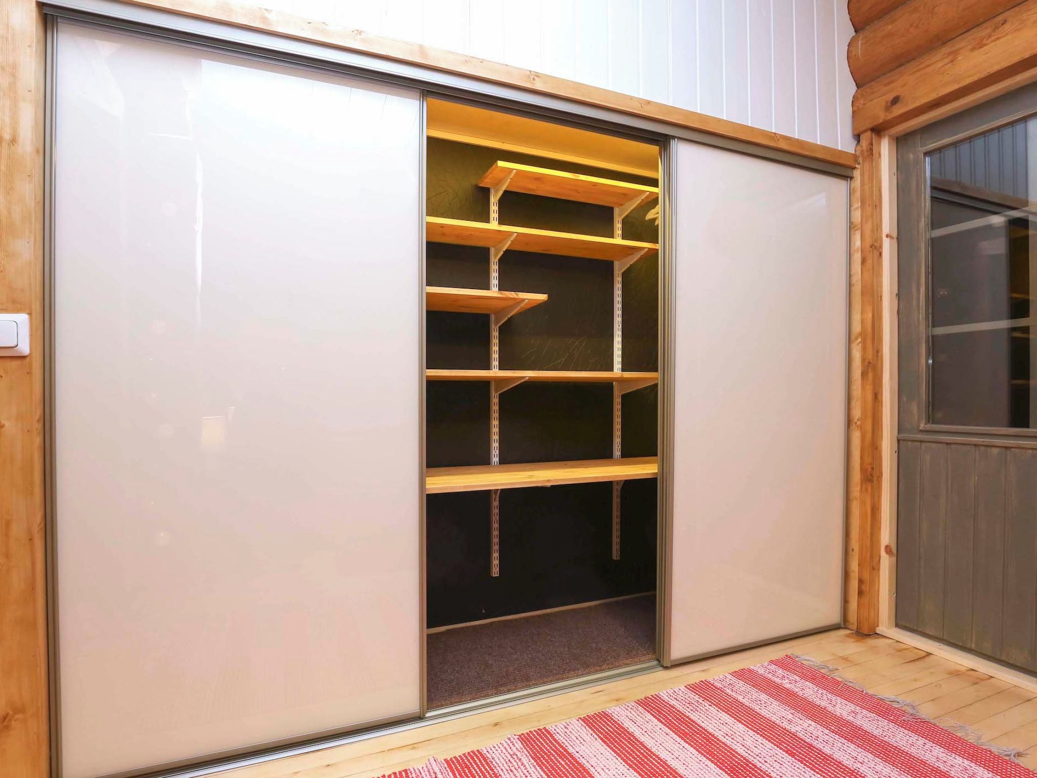 Een kamer met een schuifdeurkast, een rood-wit gestreept vloerkleed en een houten vloer.