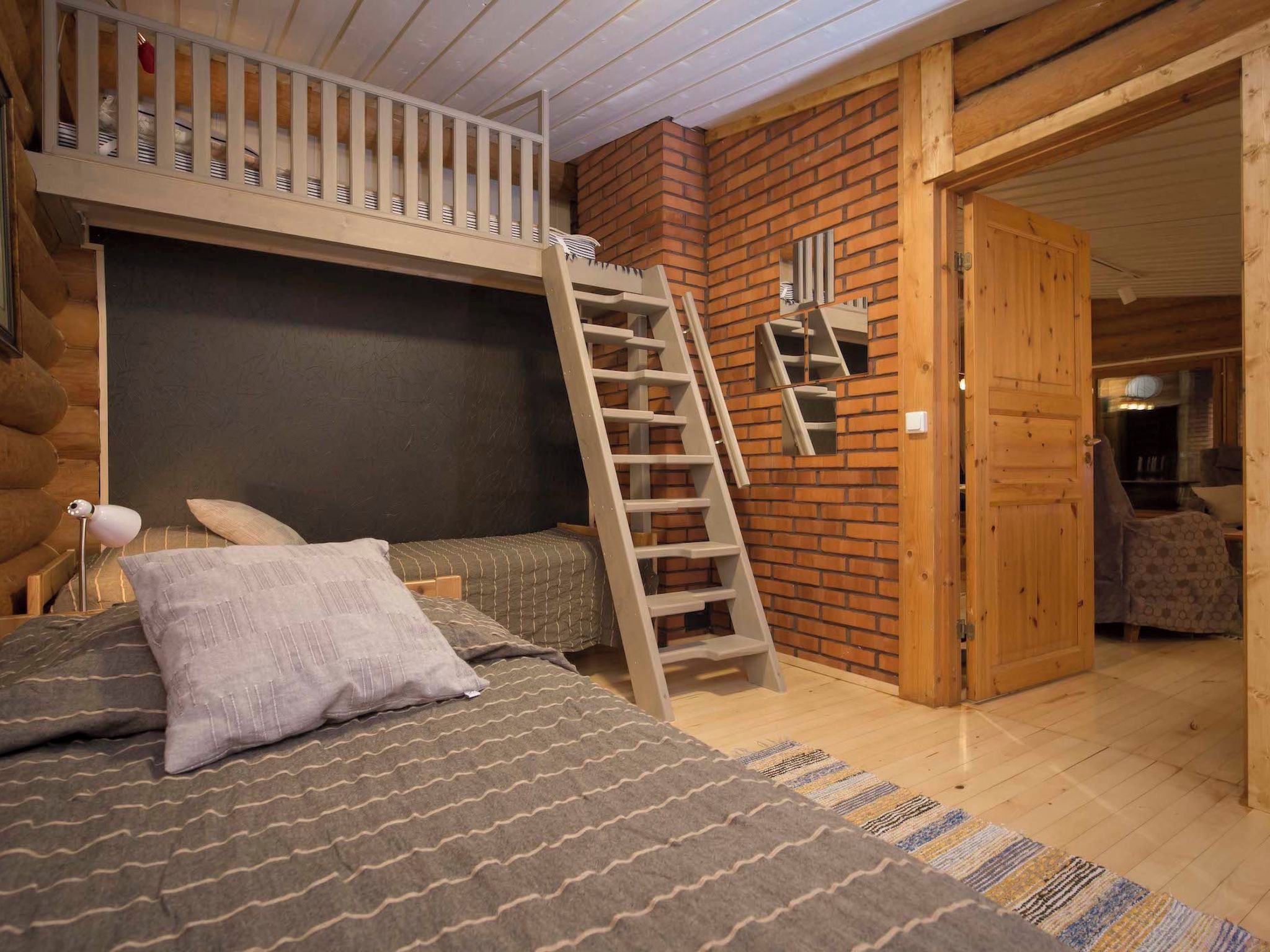A cozy log cabin bedroom with a bunk bed, a wooden ladder, and a brick wall.