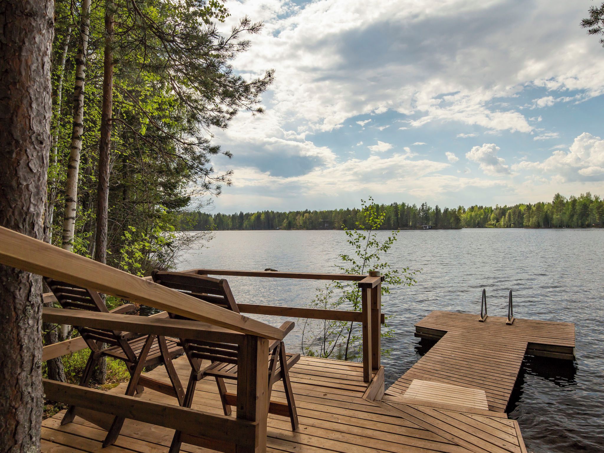 Une terrasse en bois, dotée de bancs, qui offre une vue sur un lac paisible, le tout entouré d’arbres.