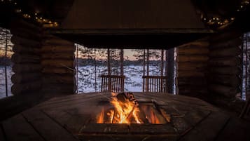 Innenansicht einer Blockhütte mit Kamin, Holzwänden und Blick auf eine verschneite Landschaft.