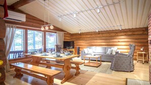 Interior de una cabaña de troncos con comedor, sofá y televisor.