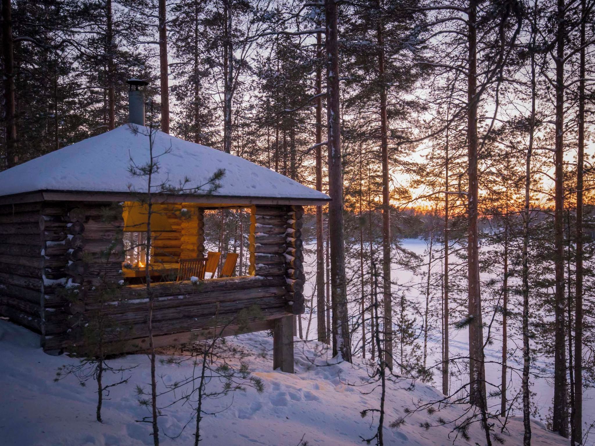 A log cabin with a snow-covered roof, surrounded by a forest.