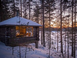 Une cabane en rondins dont le toit est recouvert de neige, entourée d’une forêt.