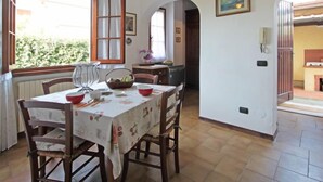 A dining area with a table set for four, a window with curtains, and a view of greenery outside. - Patrizia by Interhome (Forte dei Marmi)