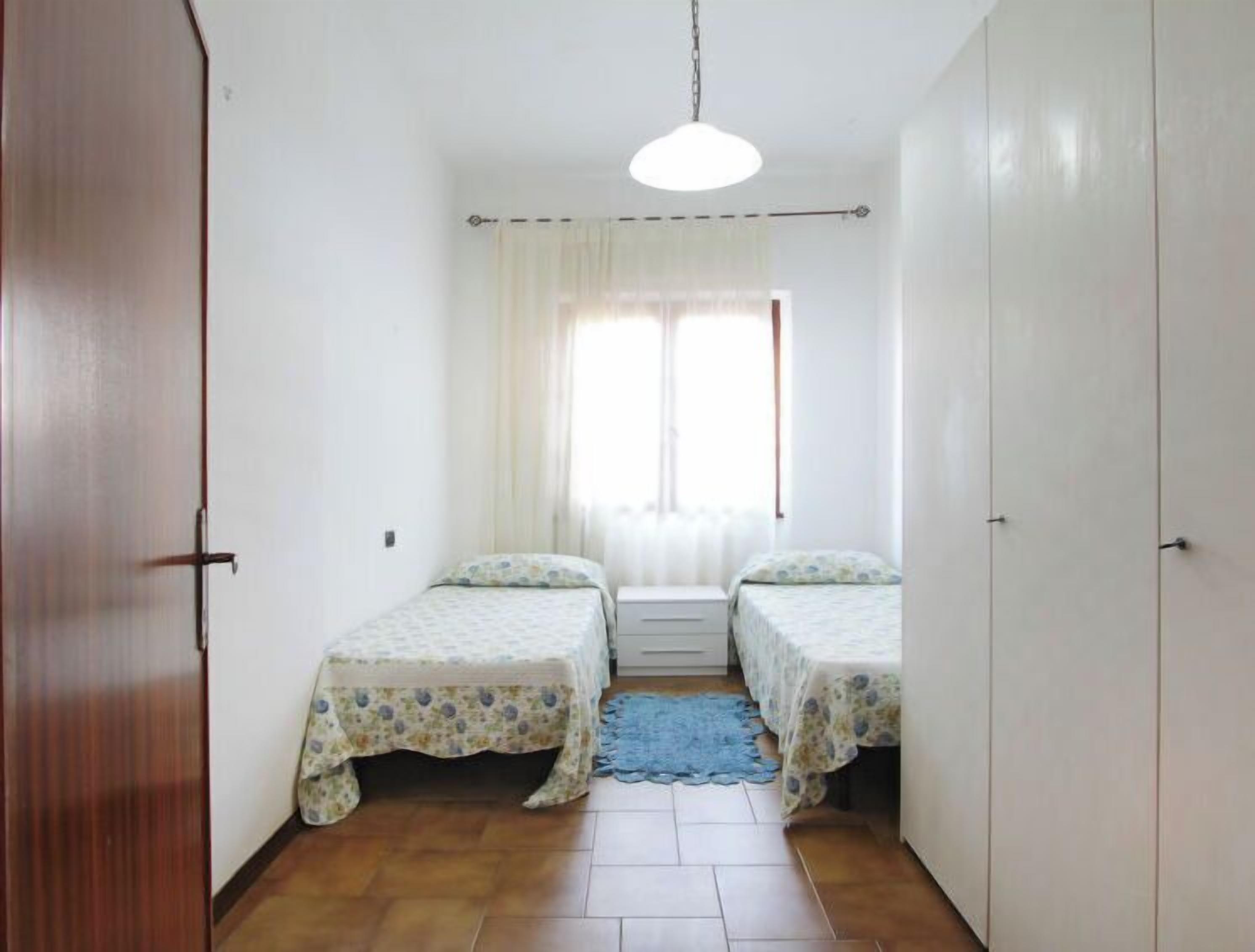 Piccola stanza stretta con due letti singoli, una porta in legno a sinistra e un armadio bianco a destra.