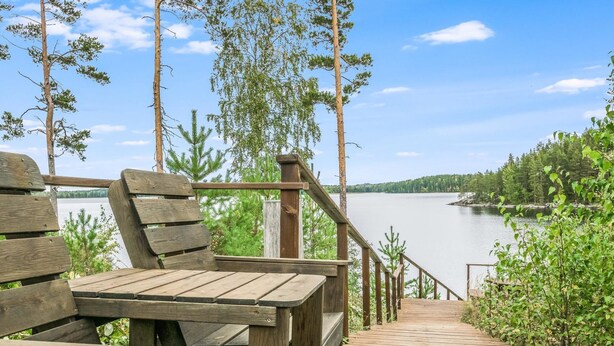 Una terraza de madera con bancos que da a un lago, rodeada de árboles.