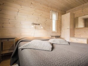 Une chambre dans un chalet en bois, avec un lit, une table de chevet, une commode et une fenêtre avec des rideaux.