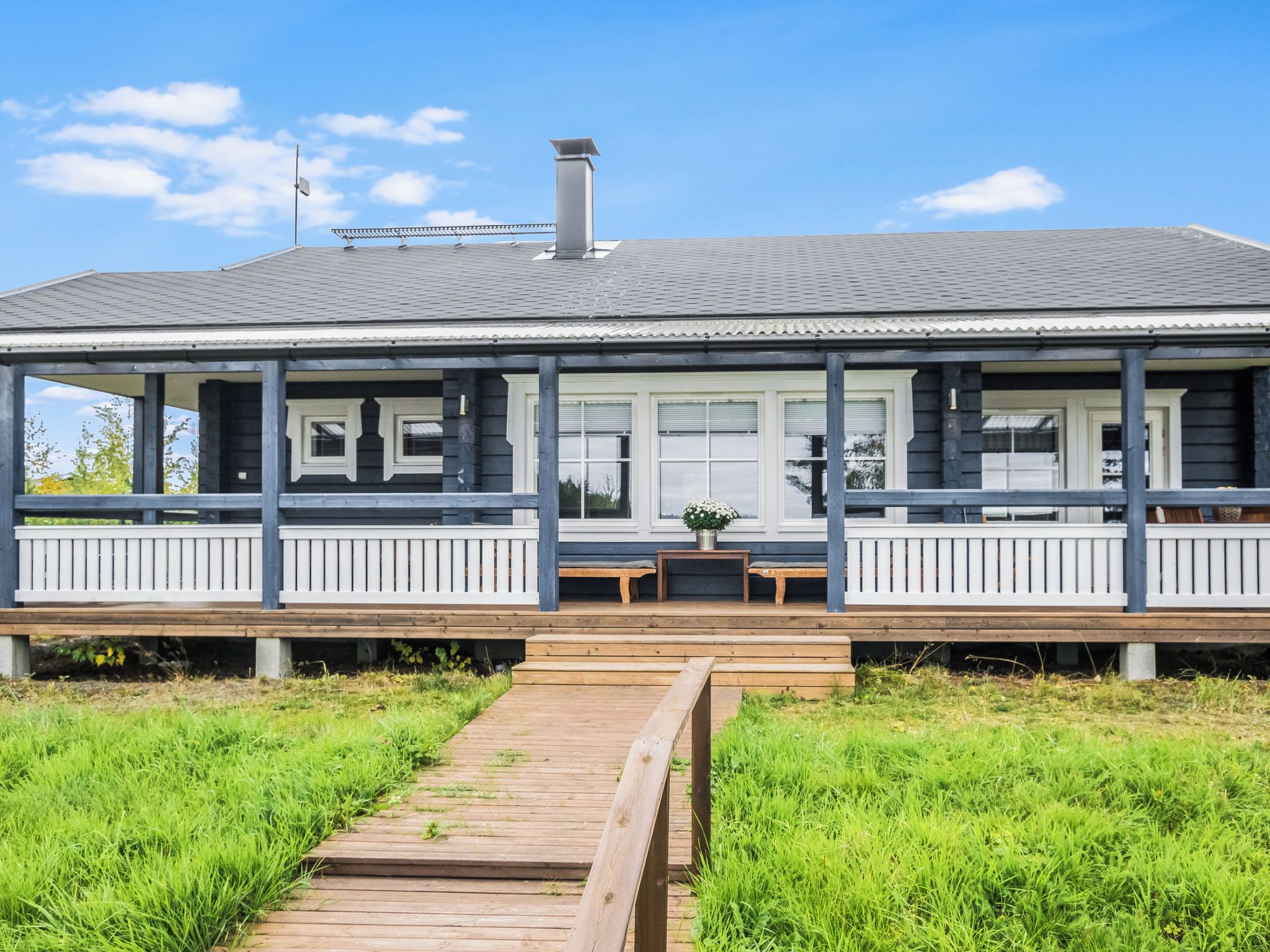 A two-story house with a covered porch, a chimney, and a wooden deck leading to the entrance.