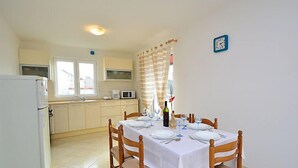 A dining area with a table set for four, a refrigerator, a microwave, and a window with curtains. - Apartment Ena by Interhome (Brodarica)