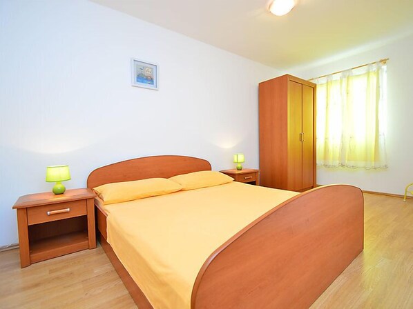 Un dormitorio con cama de madera, dos mesitas de noche con lámparas, un armario y una ventana con cortinas.