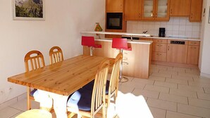 A compact kitchen with wooden cabinets, a central island with red chairs, and a dining table. - Ardévine 5 by Interhome (Ovronnaz)