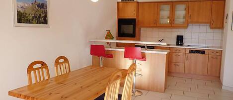 Een compacte keuken met houten kastjes, een centraal eiland met rode stoelen en een eettafel.