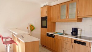 A compact kitchen with wooden cabinets, a dishwasher, a coffee maker, and a small bar area with red chairs. - Ardévine 5 by Interhome (Ovronnaz)