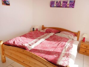 Una cama individual con estructura de madera, una colcha estampada en rosa y blanco, dos mesitas de noche con lámparas y un cuadro colgado en la pared.