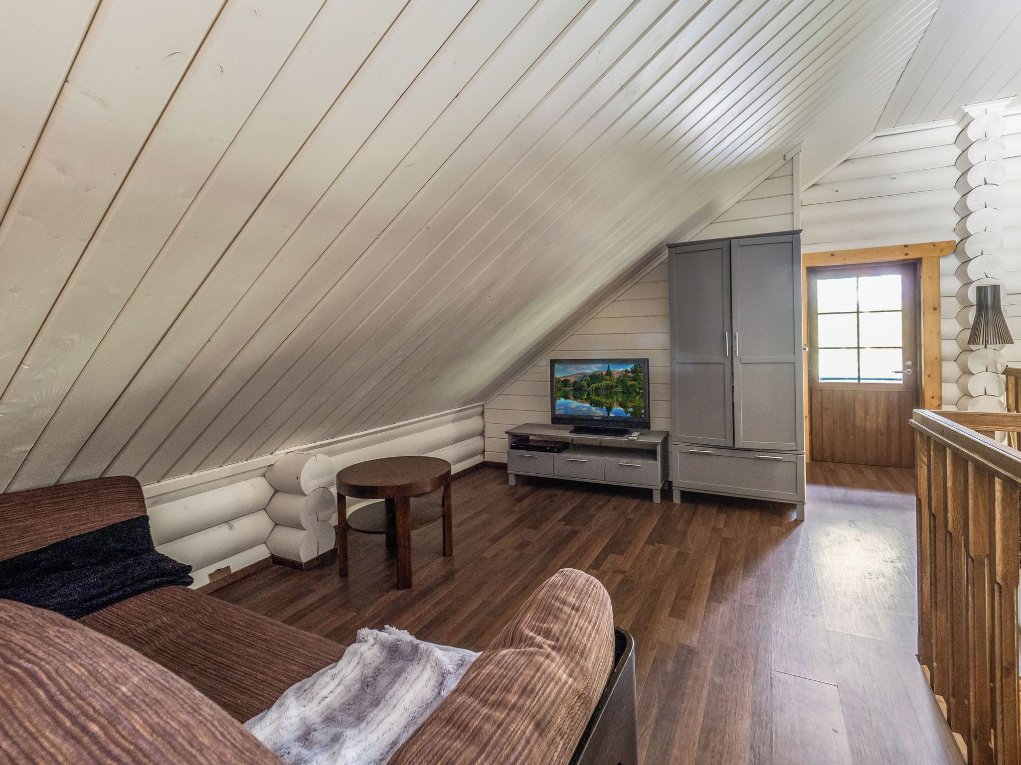 A cozy attic room with a wooden ceiling, a television, a sofa, and a cabinet.