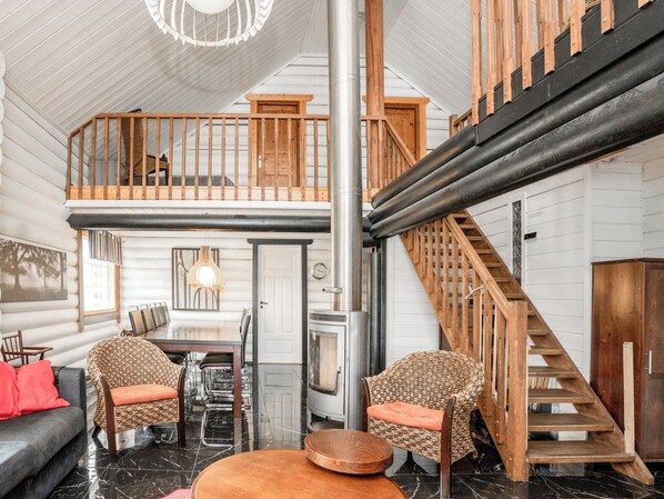 A spacious interior with a high ceiling, a dining area, a fireplace, and a wooden staircase.