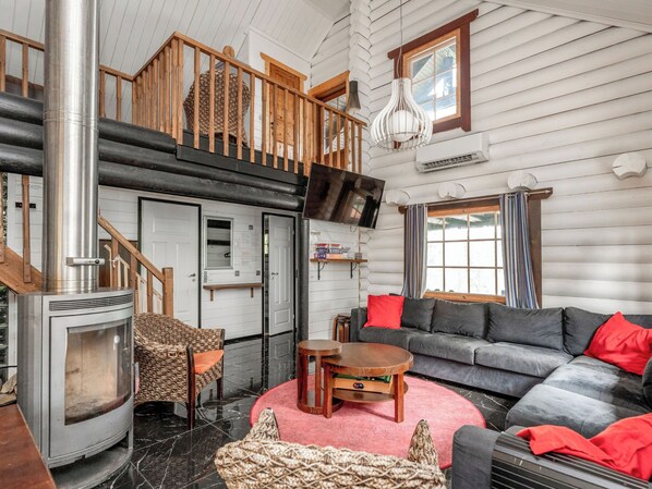 A log cabin interior with a fireplace, a sofa, a television, and a staircase.