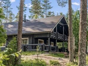 A log cabin with a porch and a chimney, surrounded by trees.