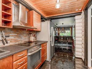 A kitchen with a brick backsplash, wooden cabinets, a stainless steel refrigerator, and a black marble floor.
