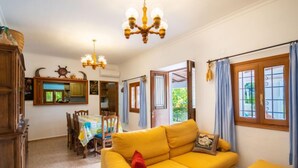 Ein helles Wohnzimmer mit einem gelben Sofa, einem Holzesstisch und einer Pendelleuchte.