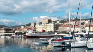 A marina with several boats docked, a large white ship with a red stripe, and a cityscape with historic buildings in the background. - Vacation home Matea by Interhome (Rijeka)