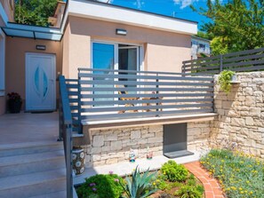 A modern building with a stone wall, a wooden bench, and a small garden area with flowers. - Vacation home Matea by Interhome (Rijeka)