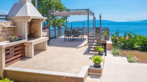 A patio with a stone barbecue, outdoor seating, and a view of the sea. - Vacation home Matea by Interhome (Rijeka)