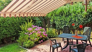 Un patio con tavolo e sedie, un pergolato e diverse piante e fiori.