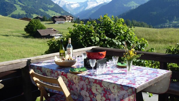 Mesa al aire libre con vistas a la montaña, una botella de vino y un cuenco de pan.