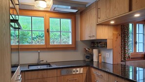 Cocina moderna con armarios de madera, encimera negra y ventana con vistas a la vegetación.