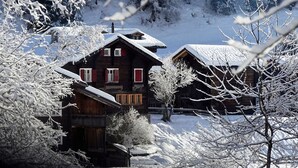 A wooden cabin with a snow-covered roof, surrounded by snow-laden trees and a clear sky. - LuxLax 2. OG Süd by Interhome (Lax)