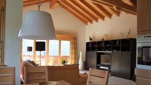 A cozy living room with a wooden ceiling, a dining table with chairs, a sofa, and a TV. - LuxLax 2. OG Süd by Interhome (Lax)