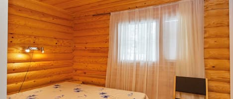 Ein Schlafzimmer einer Holzhütte mit einem Bett, einem Sessel und einem Fenster mit durchsichtigen Vorhängen.