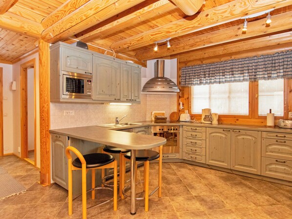 A kitchen with wooden beams, a stainless steel sink, a built-in oven, and a dining area with stools.